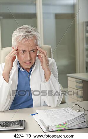 Doctor at desk rubbing his sleeves View Large Photo Image Stock Photo - Doctor at desk rubbing his sleeves . Fotosearch