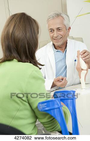 Stock Image - Doctor showing female patient artificial knee joint . Fotosearch