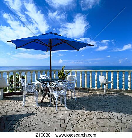Stock Image - Empty table and chairs under sunshade . Fotosearch