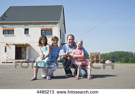 Stock Image - Family squatting in front of shell of building . Fotosearch