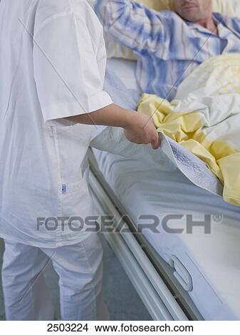 Picture - Female nurse changing bed sheet of patient's bed . Fotosearch