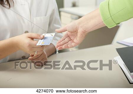 Stock Image - Female patient handing over health insurance card to doctor's assistant at desk . Fotosearch