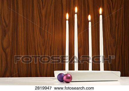 Stock Photo - Four candles burning near baubles . Fotosearch