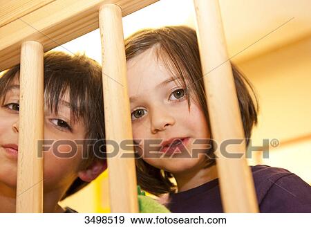 Stock Photo - Girl and boy looking through a wooden railing, low angle view . Fotosearch