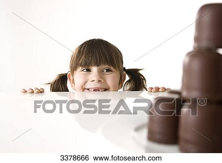 Stock Photograph - Girl looking over the edge of a table on at a plate with chocolate marshmallows . Fotosearch