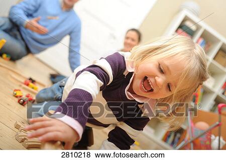 Girl playing with toys with her parents behind her View Large Photo Image Stock Photo - Girl playing with toys with her parents behind her . Fotosearch