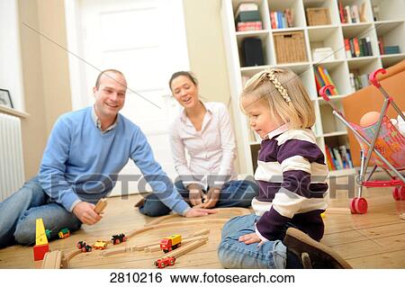 Girl playing with toys with her parents behind her View Large Photo Image Stock Photograph - Girl playing with toys with her parents behind her . Fotosearch