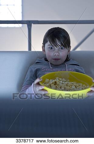 Girl sitting in front of a TV, holding bowl with popcorn, front view View Large Photo Image Stock Photo - Girl sitting in front of a TV, holding bowl with popcorn, front view . Fotosearch