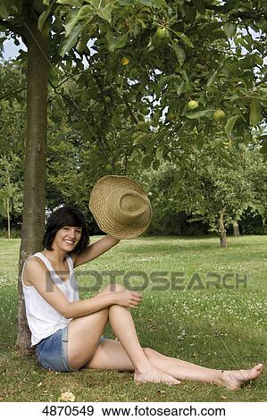 Stock Photo - Happy young woman sitting at apple tree . Fotosearch