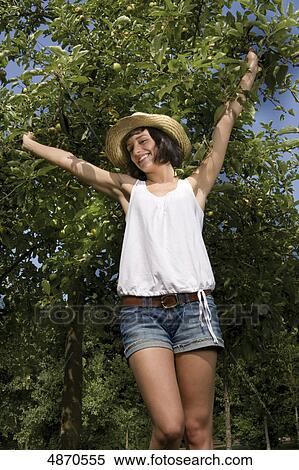 Stock Photography - Happy young woman standing at apple tree . Fotosearch