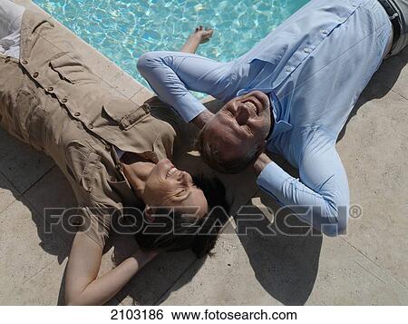 Stock Photograph - High angle view of couple lying on floor and smiling at poolside . Fotosearch