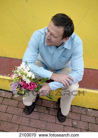 Stock Image - High angle view of man holding bouquet of flowers on street . Fotosearch