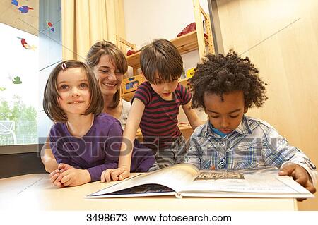 Kindergarten teacher and children looking at a book, low angle view  View Large Photo Image Stock Image - Kindergarten teacher and children looking at a book, low angle view . Fotosearch