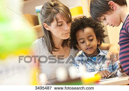 Stock Photo - Kindergarten teacher and children looking at book, low angle view . Fotosearch