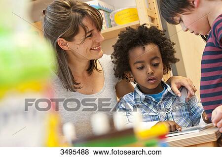 Stock Photo - Kindergarten teacher and children looking at book, low angle view . Fotosearch