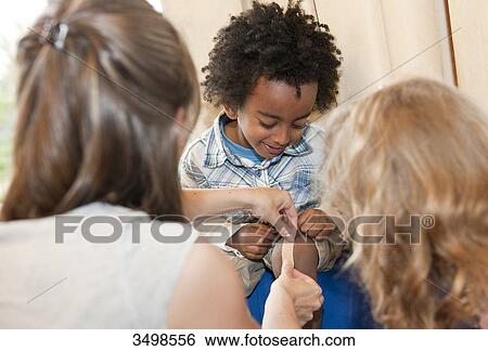 Stock Photograph - Kindergarten teacher applying a plaster on boys leg . Fotosearch