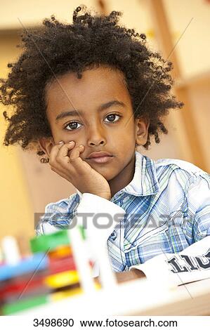 Stock Image - Little boy sitting with hand on chin, portrait . Fotosearch