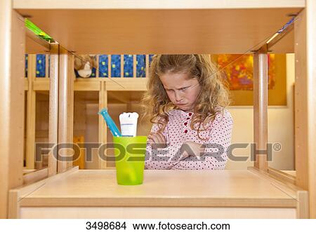Little girl crossing arms and looking at toothbrush holder on a shelf View Large Photo Image Picture - Little girl crossing arms and looking at toothbrush holder on a shelf . Fotosearch