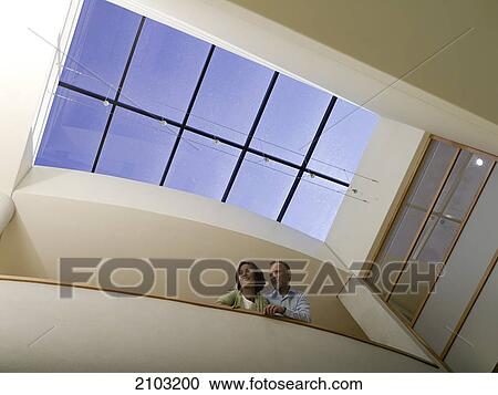 Stock Image - Low angle view of couple leaning against wall and smiling . Fotosearch