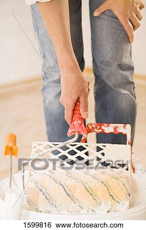 Stock Photograph - Low section view of person dipping paint roller in can . Fotosearch