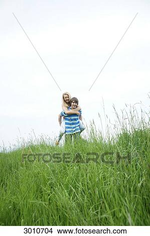 Man carrying woman piggyback through a meadow, low angle view View Large Photo Image Picture - Man carrying woman piggyback through a meadow, low angle view . Fotosearch