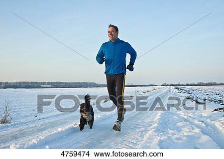 Picture - Man jogging in snow with dog, Tannheimer Tal, Tyrol, Austria . Fotosearch