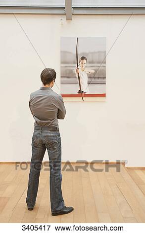 Stock Photo - Man looking at a photo on wall . Fotosearch