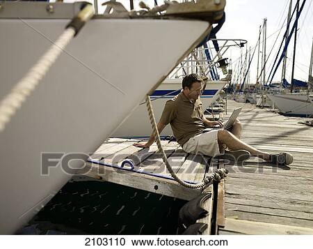 Stock Image - Man using laptop at harbor . Fotosearch
