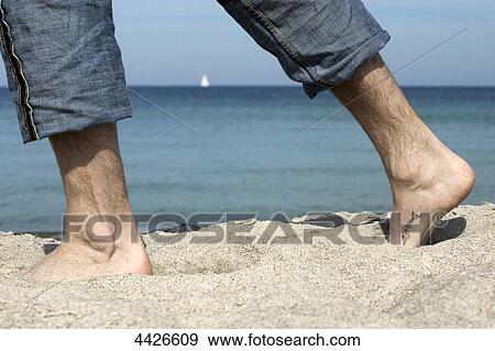 Stock Photo - Man walking barefoot at beach, lower section . Fotosearch