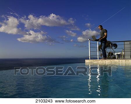 Stock Image - Man working on laptop at poolside . Fotosearch