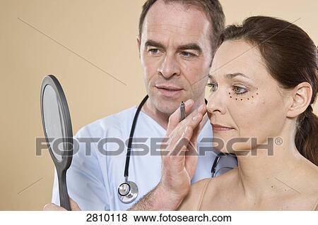 Patient looking her face in mirror with doctor View Large Photo Image Stock Photo - Patient looking her face in mirror with doctor . Fotosearch