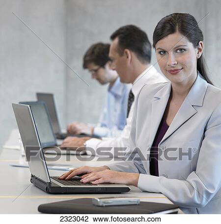 Stock Image - Portrait of businesswoman using laptop and smiling with her colleagues sitting in background . Fotosearch