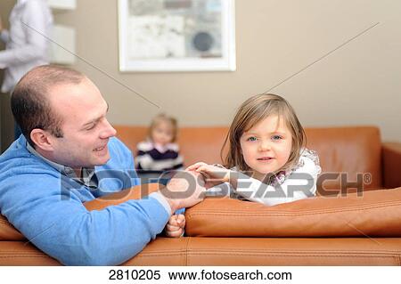 Stock Photography - Portrait of girl sitting on couch with her father . Fotosearch