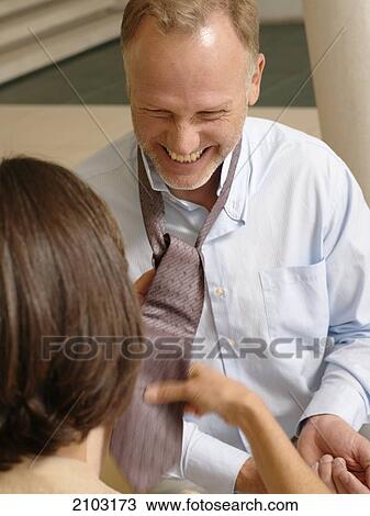 Stock Image - Rear view of woman tying her husband's tie . Fotosearch