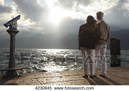 Stock Photography - Senior couple at sunset looking on water, Italy, Malcesine, Lake Garda . Fotosearch