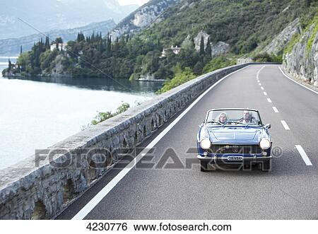 Senior couple driving convertible on coastal road, Italy, Navene View Large Photo Image Stock Photograph - Senior couple driving convertible on coastal road, Italy, Navene . Fotosearch