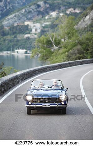 Senior couple driving convertible on coastal road, Italy, Navene View Large Photo Image Stock Photography - Senior couple driving convertible on coastal road, Italy, Navene . Fotosearch