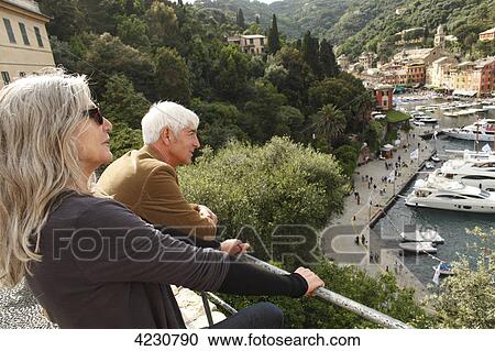 Stock Image - Senior couple looking at harbor and houses, Italy, Portofino . Fotosearch