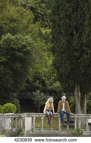 Senior couple sitting on railing in front of trees, Italy, Gardone Riviera View Large Photo Image Stock Photo - Senior couple sitting on railing in front of trees, Italy, Gardone Riviera . Fotosearch