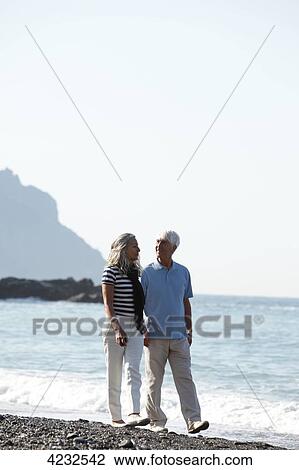 Stock Image - Senior couple walking on beach, Italy, Sori . Fotosearch
