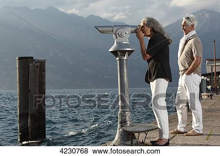 Senior couple with coin-operated binoculars looking on water, Italy, Malcesine View Large Photo Image Stock Photo - Senior couple with coin-operated binoculars looking on water, Italy, Malcesine . Fotosearch