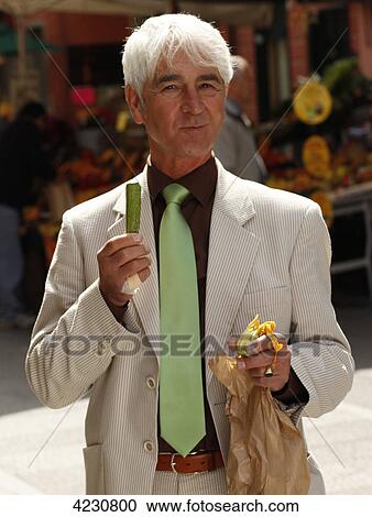 Stock Image - Senior man eating vegetables in town, Italy, Rapallo . Fotosearch