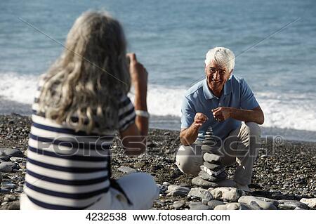 Stock Photo - Senior woman taking picture of man on beach, Italy, Sori . Fotosearch