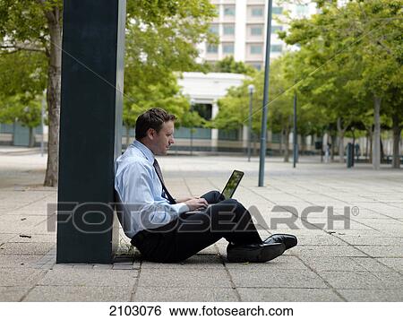 Side profile of businessman sitting at roadside and using laptop View Large Photo Image Stock Photograph - Side profile of businessman sitting at roadside and using laptop . Fotosearch