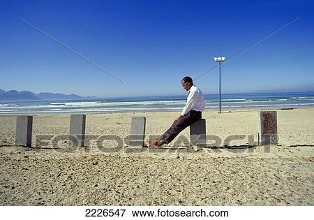 Side profile of businessman sitting on concrete pole at beach View Large Photo Image Stock Photo - Side profile of businessman sitting on concrete pole at beach . Fotosearch