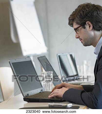 Stock Image - Side profile of businessman using laptop in office . Fotosearch