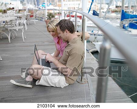 Picture - Side profile of couple using laptop at harbor . Fotosearch