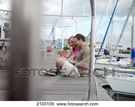 Stock Photography - Side profile of couple using laptop at harbor . Fotosearch