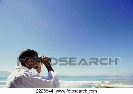 Picture - Side profile of man looking through binoculars on beach . Fotosearch