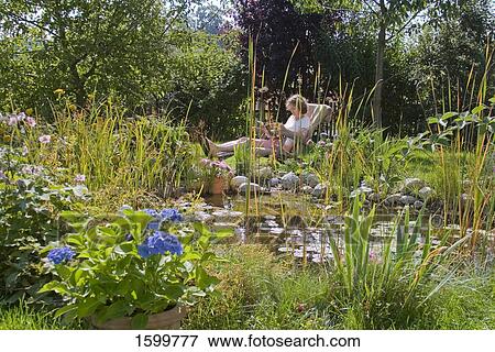 Stock Photo - Side profile of woman reading magazine on lounge chair in lawn . Fotosearch